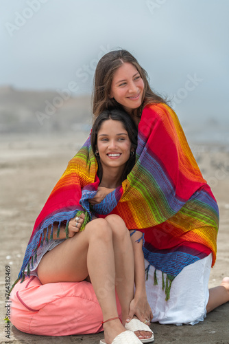Friends sitting on the beach wrapping in colorful blanket