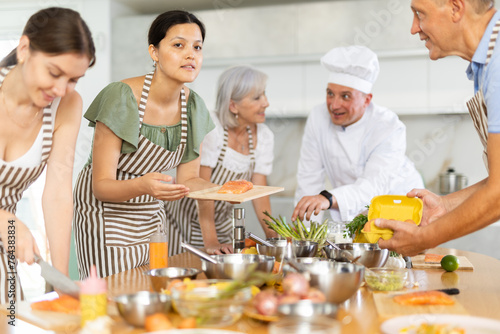 Chef in cook uniform teaches cooking class students how to clean and cut salmon fillet