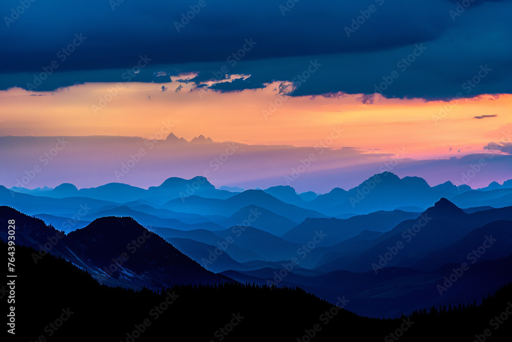 Dark silhouettes of mountains against the sky at sunset with dark clouds. A panoramic view of distant mountain peaks in black silhouettes against the background of a blue and orange twilight sky.