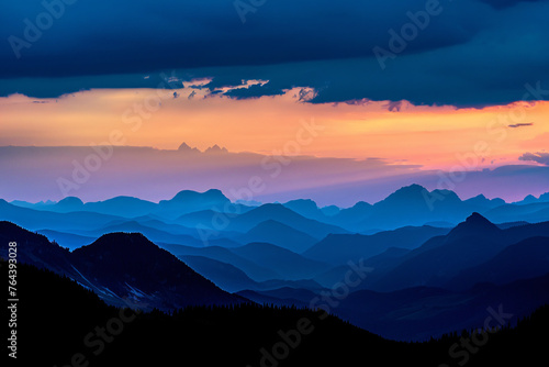 Dark silhouettes of mountains against the sky at sunset with dark clouds. A panoramic view of distant mountain peaks in black silhouettes against the background of a blue and orange twilight sky.