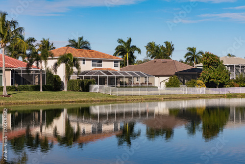 Typical concrete house on the shore of a lake in southwest Florida in the countryside with palm trees, tropical plants and flowers, lawn and pine trees. Florida. © murmakova
