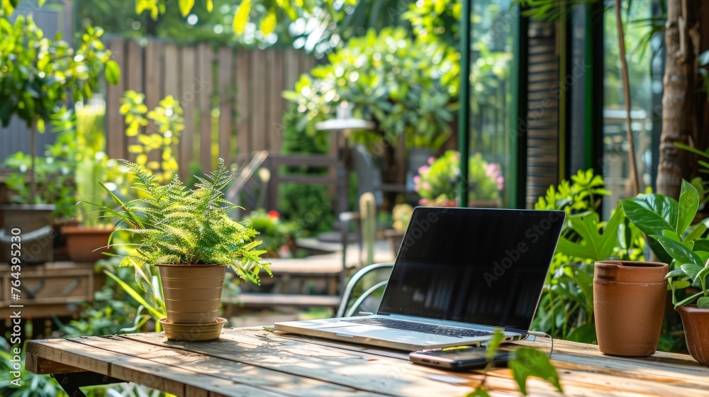 A laptop with stands on a wooden table in the courtyard of a beautiful home garden,