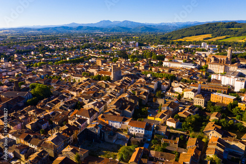 Aerial view of residential areas of Pamiers town with similar brownish roofs in green valley of Ariege River on summer day, Occitanie