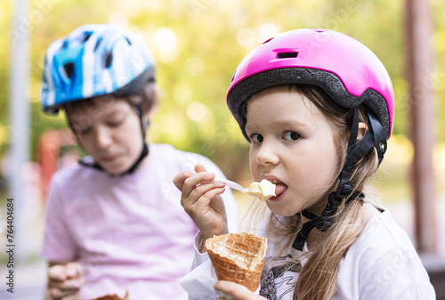 Young girl and boy eating ice cream and wearing helmets