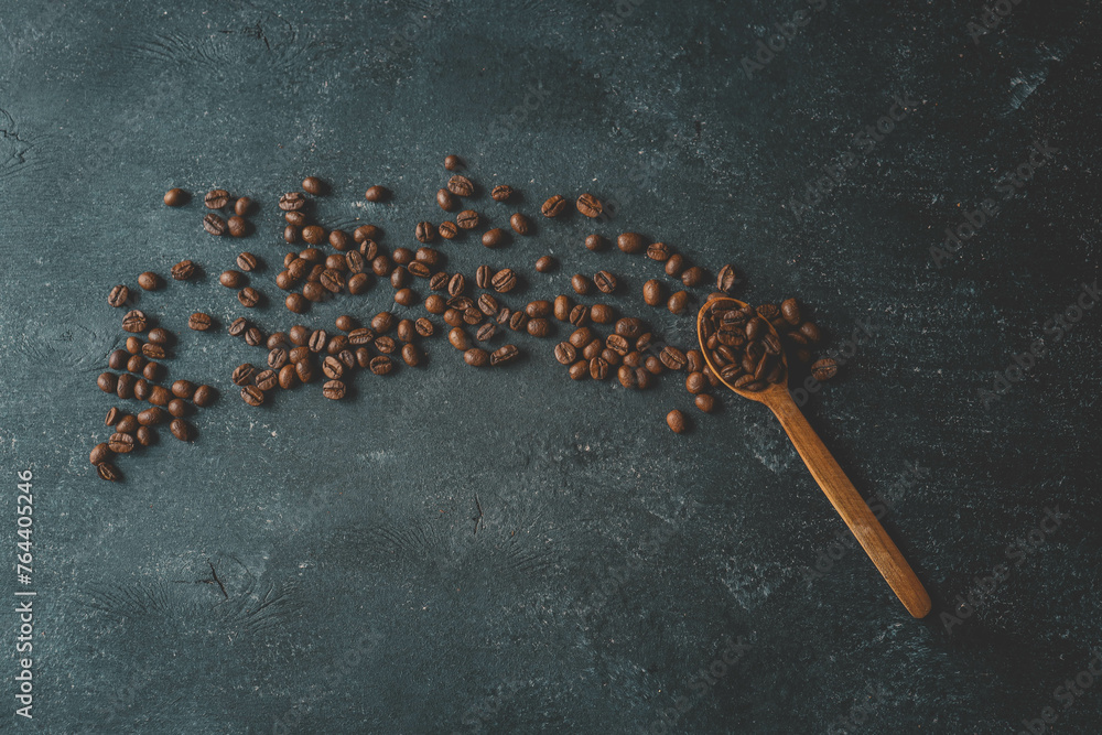 Coffee beans pour out from a wooden spoon on a retro background, top view Coffee beans pour out from a wooden spoon on a retro background, top view