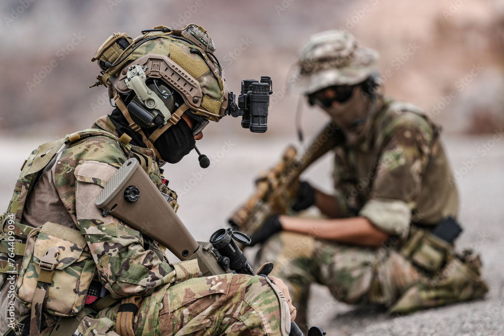 Fototapeta premium Soldiers in camo gear during a tactical operation with binoculars and rifles on a rocky terrain, showcasing military precision and readiness.