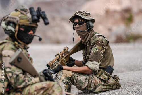 Soldiers in camo gear during a tactical operation with binoculars and rifles on a rocky terrain, showcasing military precision and readiness.