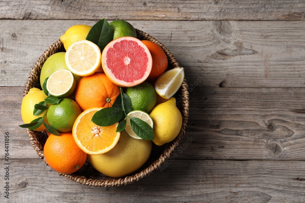 Different fresh citrus fruits and leaves in wicker basket on wooden table, top view. Space for text - obrazy, fototapety, plakaty 