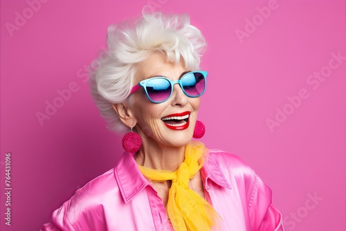 Portrait of beautiful smiling senior woman in pink jacket and sunglasses on pink background © Chacmool