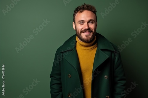 Handsome bearded man in green coat and yellow sweater smiling at the camera