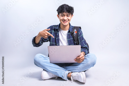 Foto Full length view of young Asian student male sitting cross legged, pointing at l
