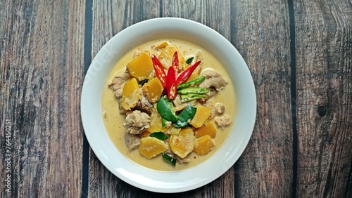 Red curry chicken with pumpkin and coconut milk in white bowl on wooden table. Authentic Thai food.