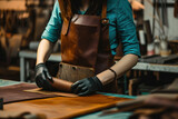 Craftswoman creating leather product in workshop wearing apron and gloves