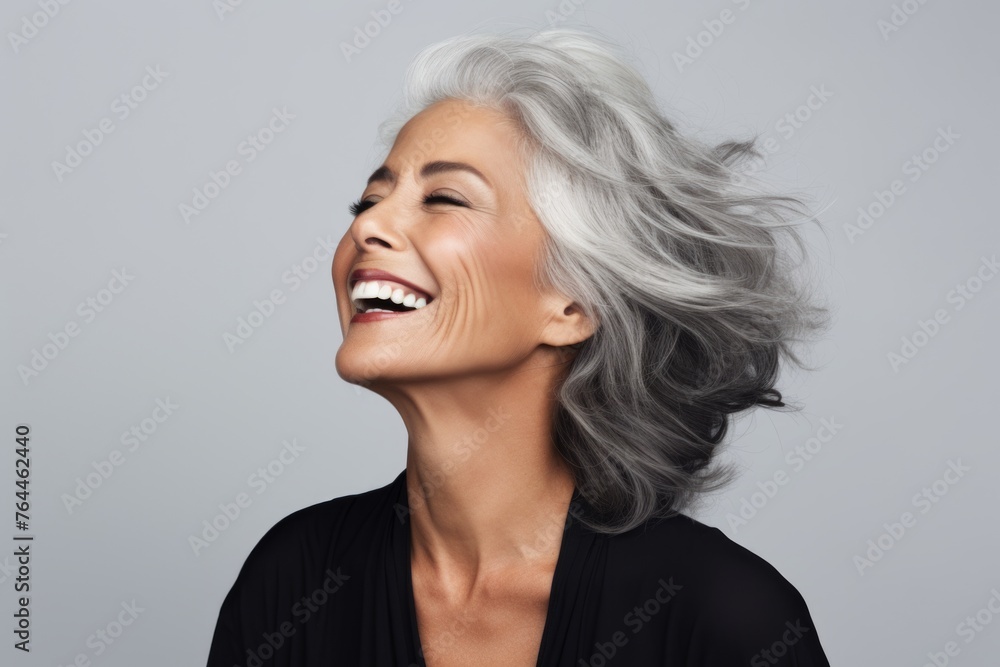 Portrait of happy senior woman laughing and looking up against grey background Portrait of happy senior woman laughing and looking up against grey background
