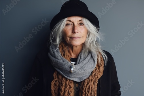 Portrait of senior woman wearing hat and scarf against grey background.