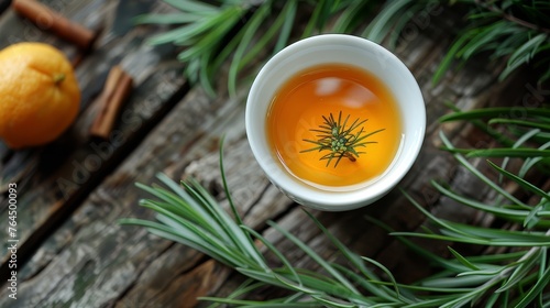  A cup of tea sits atop a wooden table, near two oranges and a pine tree branch