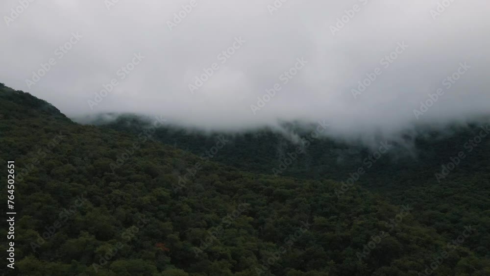 Ominous weather wit low clouds collecting on the mountainside creating a mysterious atmosphere over a dense forest, aerial drone footage Ominous weather wit low clouds collecting on the mountainside creating a mysterious atmosphere over a dense forest, aerial drone footage