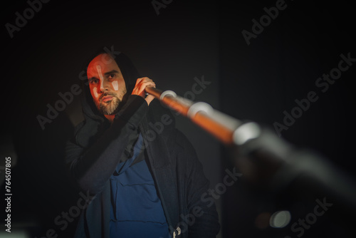 Valmiera, Latvia - March 15, 2024 - A focused individual with face paint plays the didgeridoo, illuminated by soft lighting against a dark background.