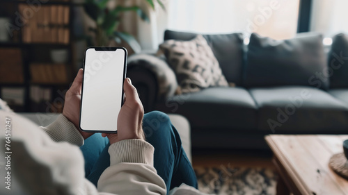 a person holding an SmartPhone with a white screen, sitting on the couch in their living room, mockup photo