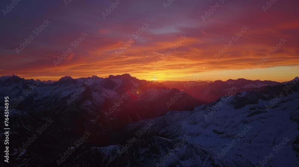 Majestic mountains silhouetted against a fiery sunset sky. The peaks are capped with snow,