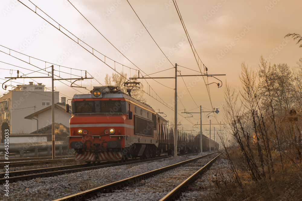 Freight train with red locomotive and some waggons is driving towards the camera in a mystical early morning setting ith sun about to rise. Freight train with red locomotive and some waggons is driving towards the camera in a mystical early morning setting ith sun about to rise.