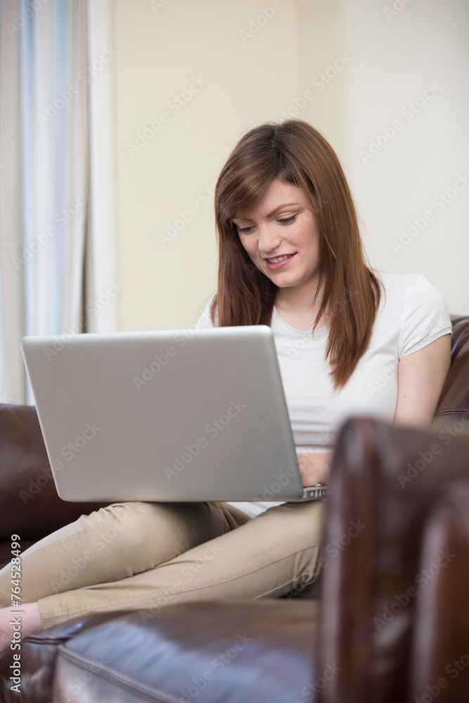 Happy young woman working on her laptop at home on sofa. Happy young woman working on her laptop at home on sofa.