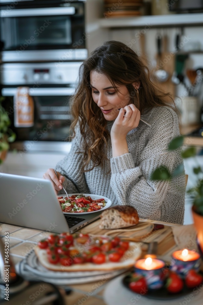 A woman sitting at a table with a laptop and a plate of food. Suitable for illustrating working from home or enjoying a meal while working
