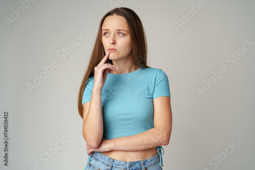 Portrait of thoughtful uncertain young casual girl on gray background