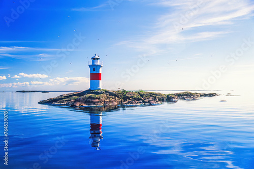 Lighthouse on a rocky islet with reflections in the water a sunny summer day photo