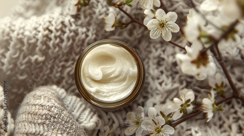 Creamy face cream in jar with blooming branches on knitted background 