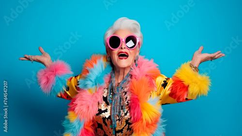 Stylish senior woman in colorful attire with oversized pink sunglasses against a blue background, embodying fun and confidence.