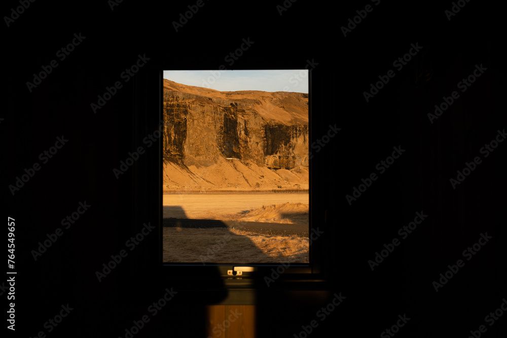 A serene view through a window frame the warm glow of sunset on desert cliff highlighting the beauty of arid landscape with light and shadow at cabin home in Iceland