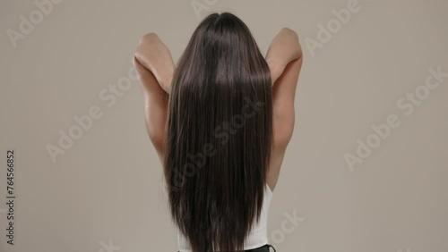 Brunette girl with long straight hair, rear view in the studio on a light background.