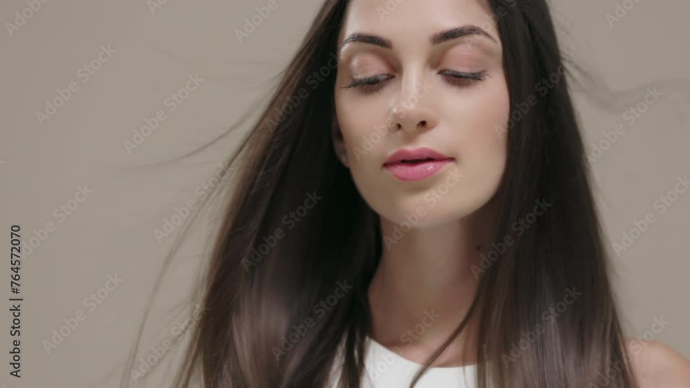 A brunette girl with long straight hair poses in the studio against a light background.