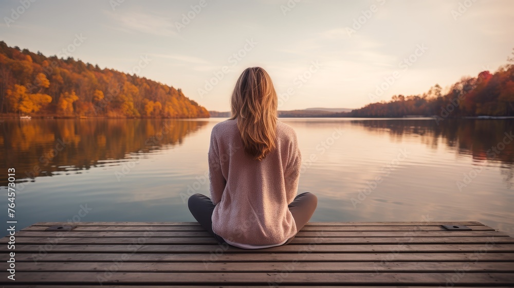 Young woman outdoors on the pier in calm morning meditation by the lake.