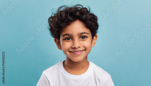 Portrait of amazing cheerful little boy with curly hairdo in white T-shirt looking at camera with happy carefree smile and missed milk teeth. indoor studio shot isolated on blue background