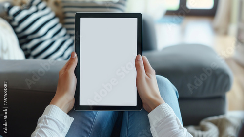 A woman holding an SmartPad with a white screen, sitting on the couch in her living room with a close up shot of the tablet screen and a blurred background in the style of a mockup