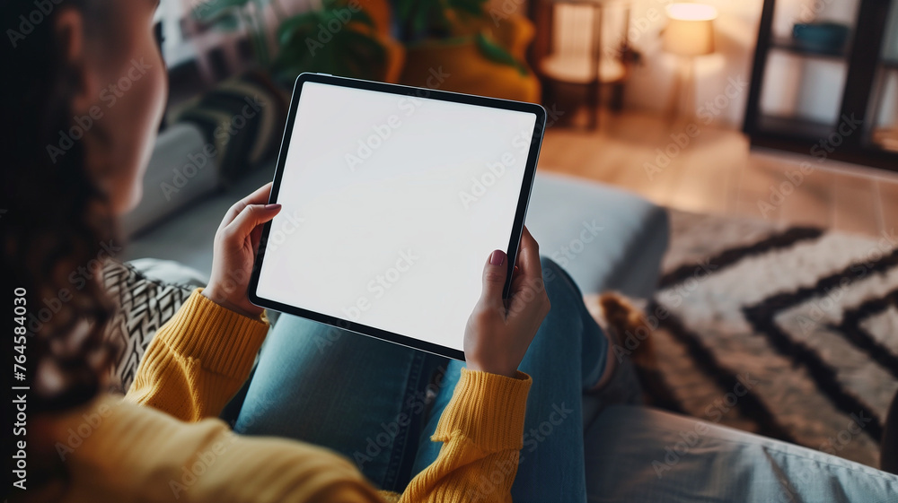 A woman holding an SmartPad with a white screen, sitting on the couch in her living room with a close up shot of the tablet screen and a blurred background in the style of a mockup