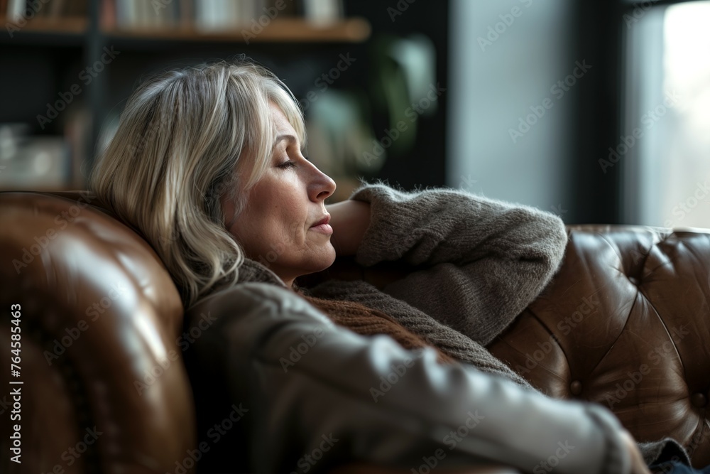 Depressed middle-aged woman in her forties, sitting on a sofa. Middle age crisis, depression, divorce concept. Depressed middle-aged woman in her forties, sitting on a sofa. Middle age crisis, depression, divorce concept.