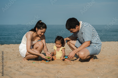 toddler baby girl playing sand toy with father and mother. happy family on the sea beach