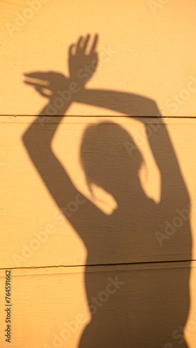 Shadow silhouette of a young woman dancing hands up in morning sunlight. Shade of a girl on house wall outside. Concept of rest, relax, peace, dance, home, lifestyle, aesthetic, freedom, joy routine.