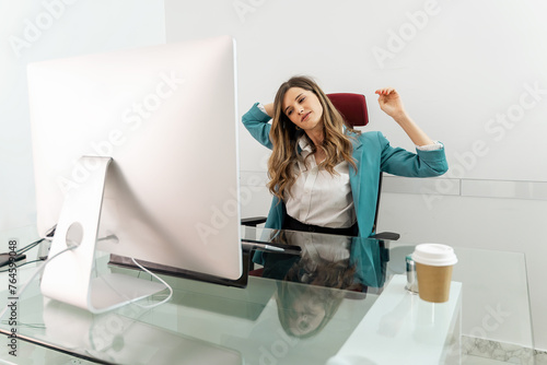 Obraz na plátne A professional woman - stretching during a break at office desk - embodying work-life balance - employee wellbeing in casual corporate environment, reflecting ease and efficiency and a busy schedule