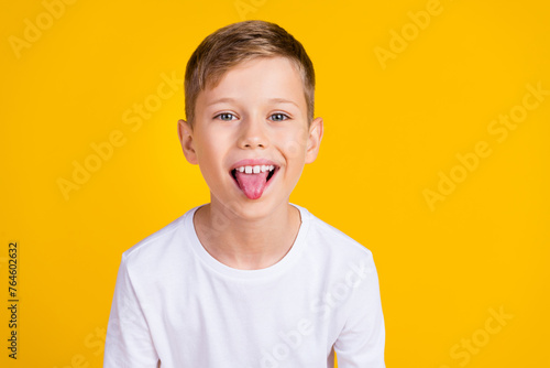 Photo of carefree funky boy wear white shirt stick out teasing you empty space isolated yellow color background