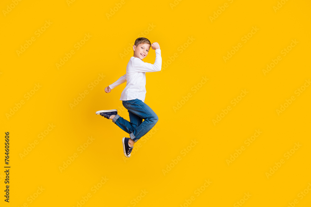 Full length photo of cool lucky boy wear white shirt rising fists jumping high empty space isolated yellow color background