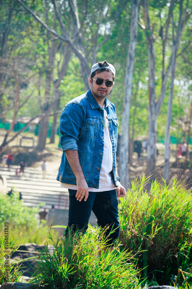 Close up shot of a model, posing with denim jacket and black sunglasses with selective focus. Handsome indian model standing in nature. Smart, dashing indian men in fashionable outfit. Close up shot of a model, posing with denim jacket and black sunglasses with selective focus. Handsome indian model standing in nature. Smart, dashing indian men in fashionable outfit.
