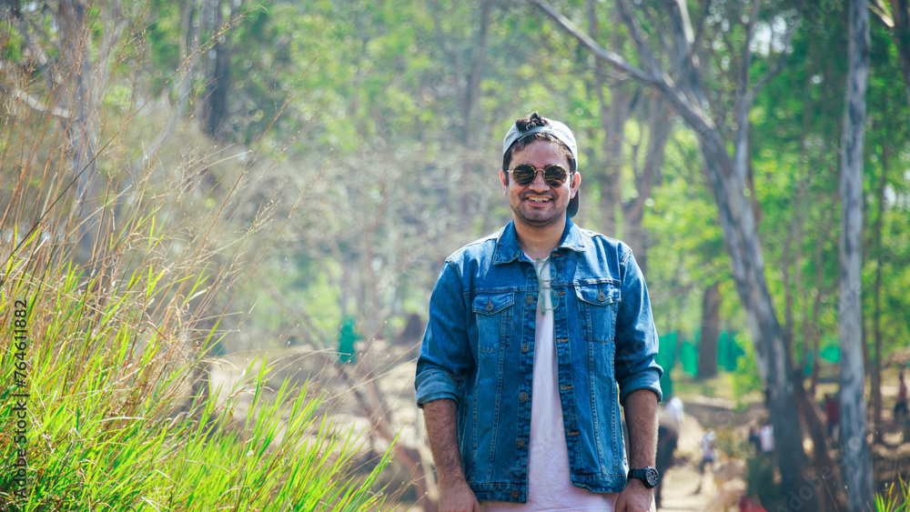 Close up shot of a model, posing with denim jacket and black sunglasses with selective focus. Handsome indian model standing in nature. Smart, dashing indian men in fashionable outfit.