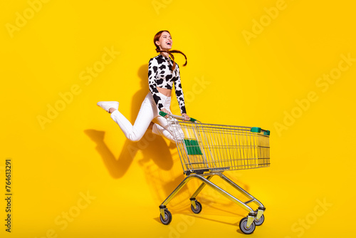Full size photo of crazy overjoyed girl jump push mall market trolley isolated on yellow color background