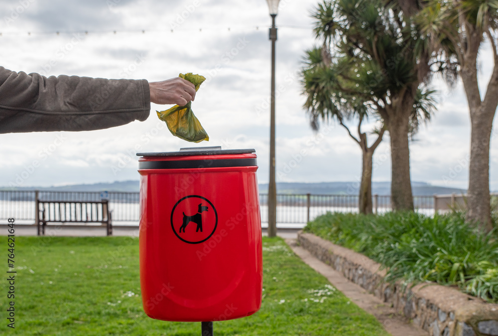 Dog poop bin. A hand placing a poo bag into a red waste bin for dog poo disposal. Park bin with