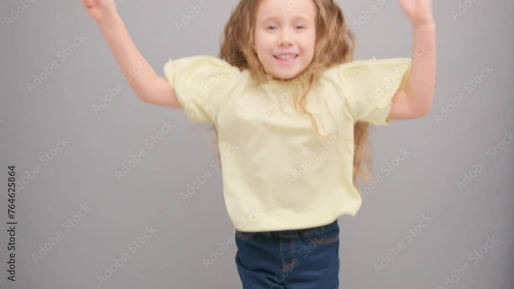 Little curly happy girl jumps and rejoices. In the studio on a gray background. Little curly happy girl jumps and rejoices. In the studio on a gray background.