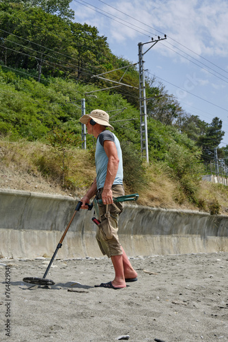 A man with a metal detector on a sandy beach in the daytime in summer.